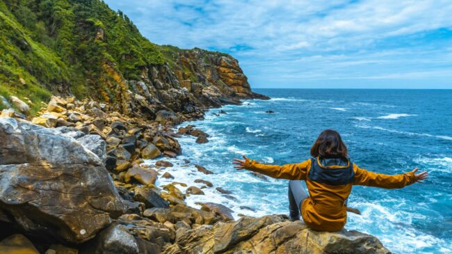 A female model sitting on the shore and looking with satisfaction to the beautiful sea along the Garden Route, South Africa