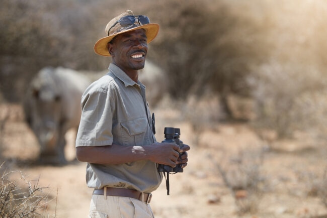 Portrait of a confident game ranger looking at a group of rhinos in the veld.