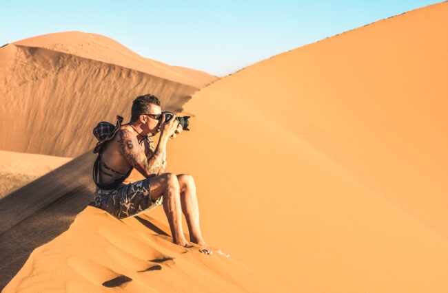 Solo man photographer sitting on sand at Dune 45 in Sossusvlei - Adventure travel to African wonders in Namibia