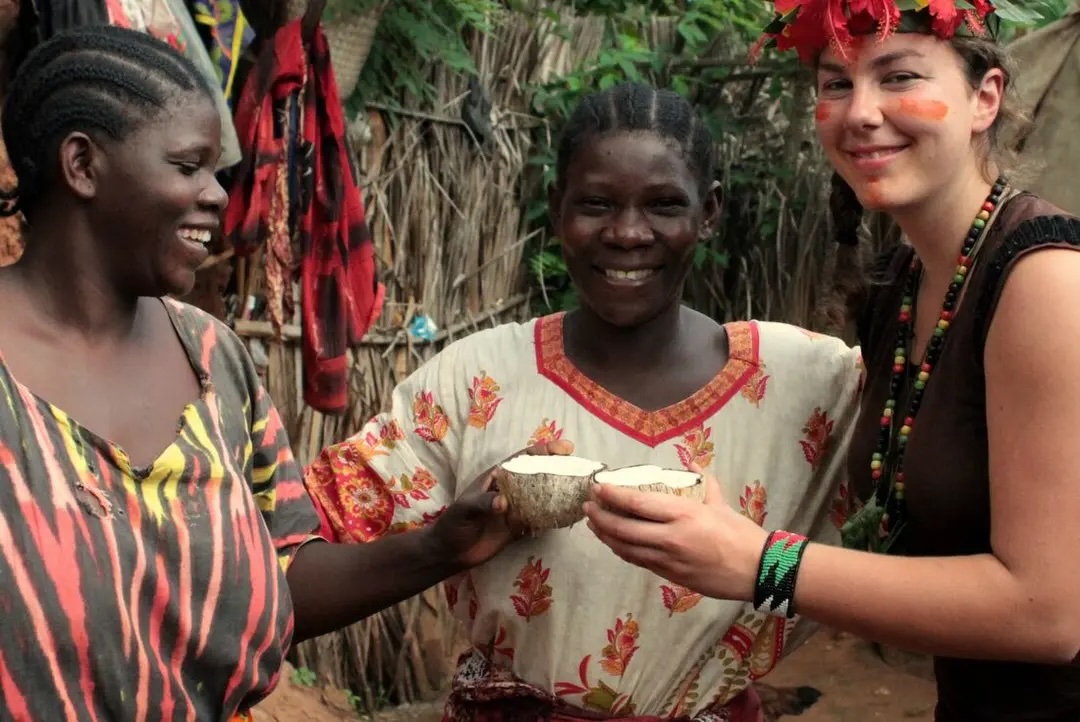 Young woman drinks from a coconut with local women in Zanzibar.