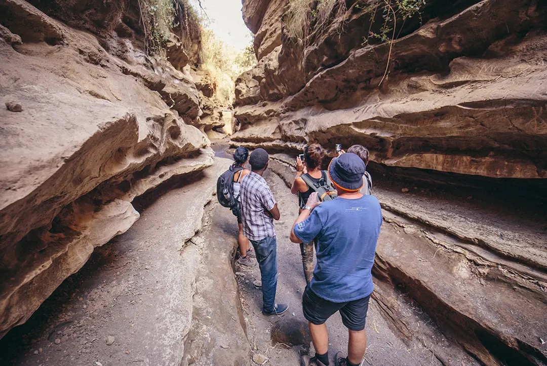 Group photographs rock formation as they walk between crevice's.