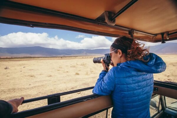 Woman wearing blue jacket photographs animals from safari vehicle.