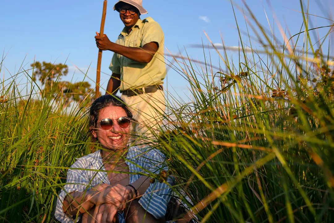 Woman smiles as local poler takes her through Okavango waterways in a mokoro.