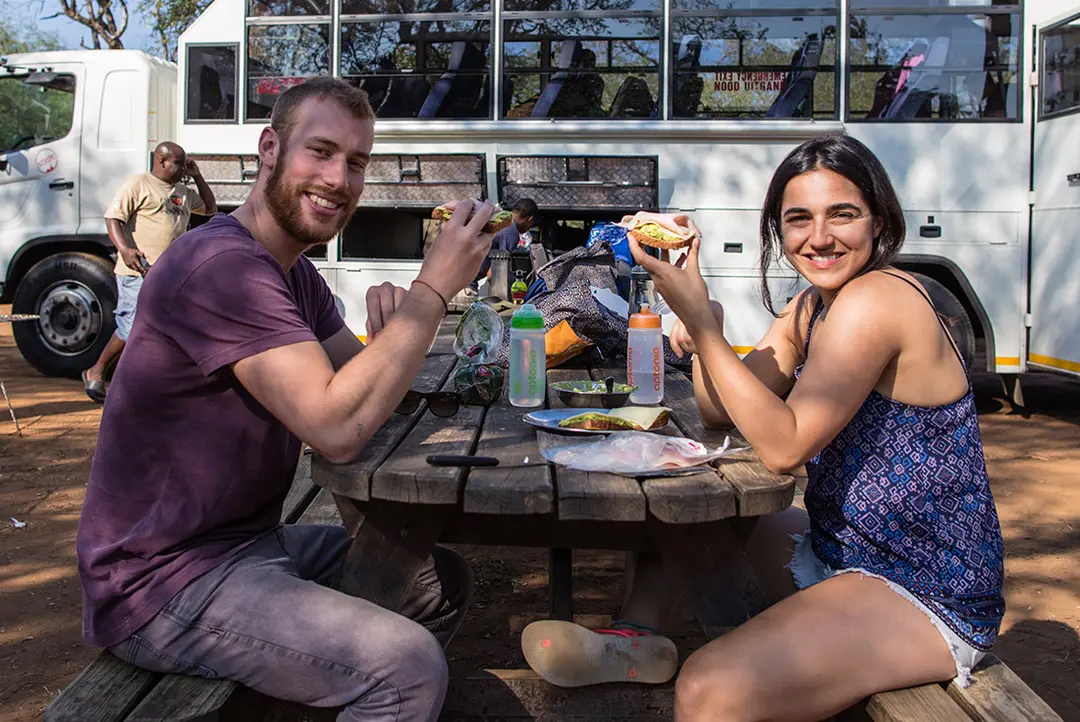 Couple enjoy lunch on a picnic bench beside overland truck.