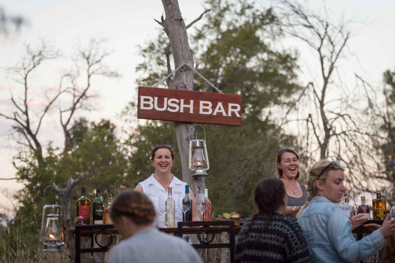 Group of happy women drinking under bush bar sign in Kruger National Park.