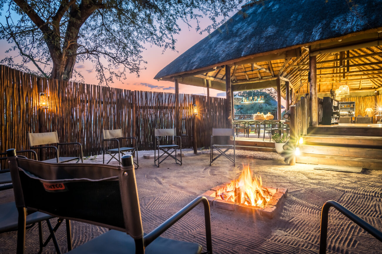 Camping chairs placed around burning fire at safari lodge.